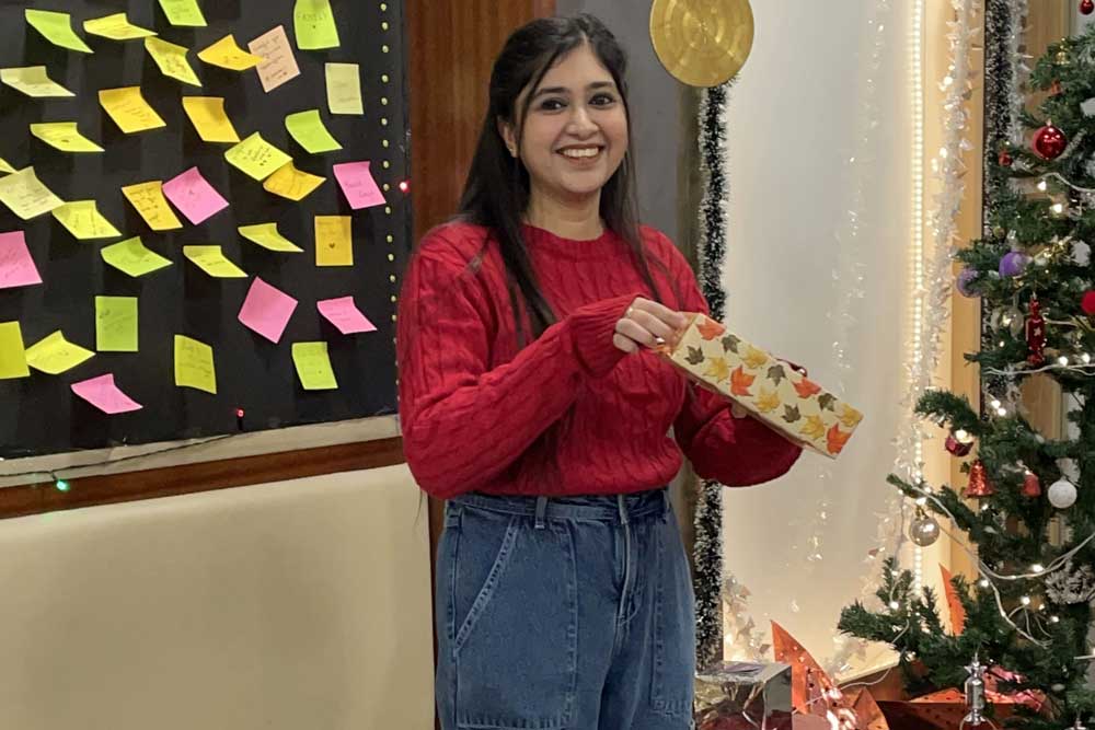 A girl is opening a gift while standing and smiling
